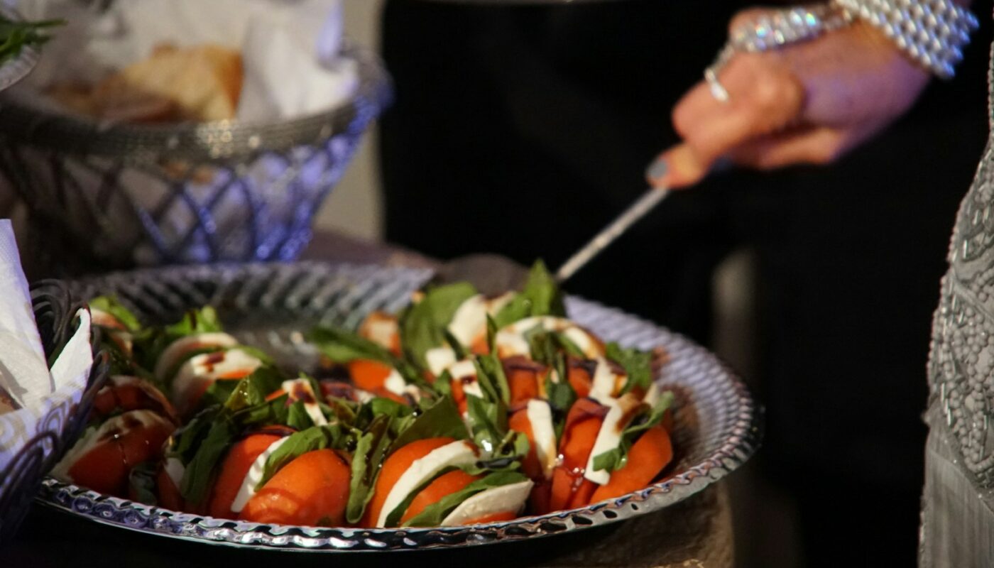 person holding stainless steel fork and knife slicing tomato on black ceramic bowl